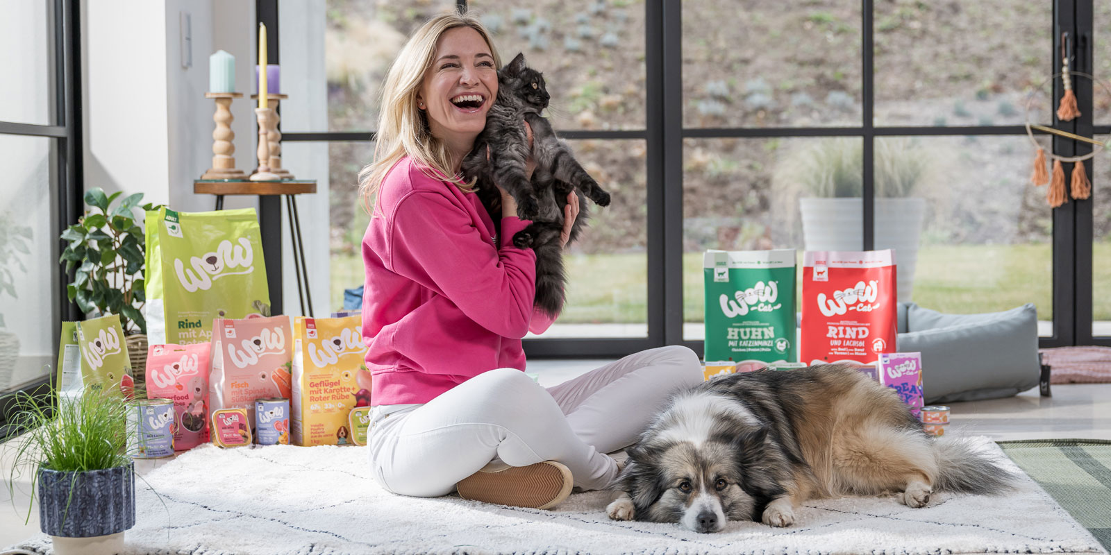 Katharina Miklauz sitzt auf dem Boden mit einer Katze in den Armen und einem Hund der vor ihren Füßen liegt